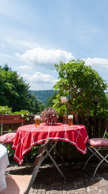 Ein runder Tisch mit roter Tischdeck und zwei Stühlen stehen im Biergarten mit traumhafter Aussicht. | © Ofenstüberl