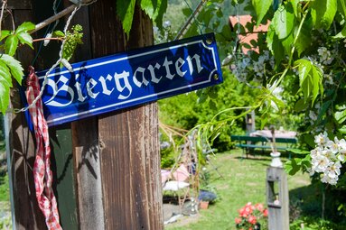 Blau-weißes Schild mit der Aufschrift "Biergarten" an einem Pfosten im Garten. | © Ofenstüberl