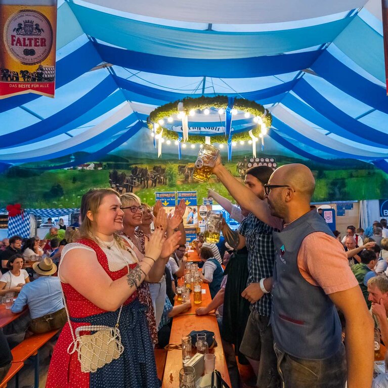Menschen in Tracht stehen in einem Bierzelt auf Bierbänken und feiern. | © Bodenmais Tourismus & Marketing GmbH