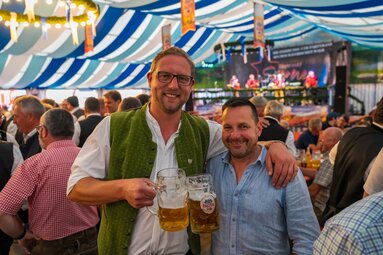 Im Bierzelt stoßen zwei Männer in Tracht mit ihren halbvollen Maßkrügen an. | © Bodenmais Tourismus & Marketing GmbH