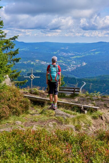 Eine Frau steht neben einem kleinen Gipfelkreuz und genießt die Aussicht. | © Bodenmais Tourismus & Marketing GmbH